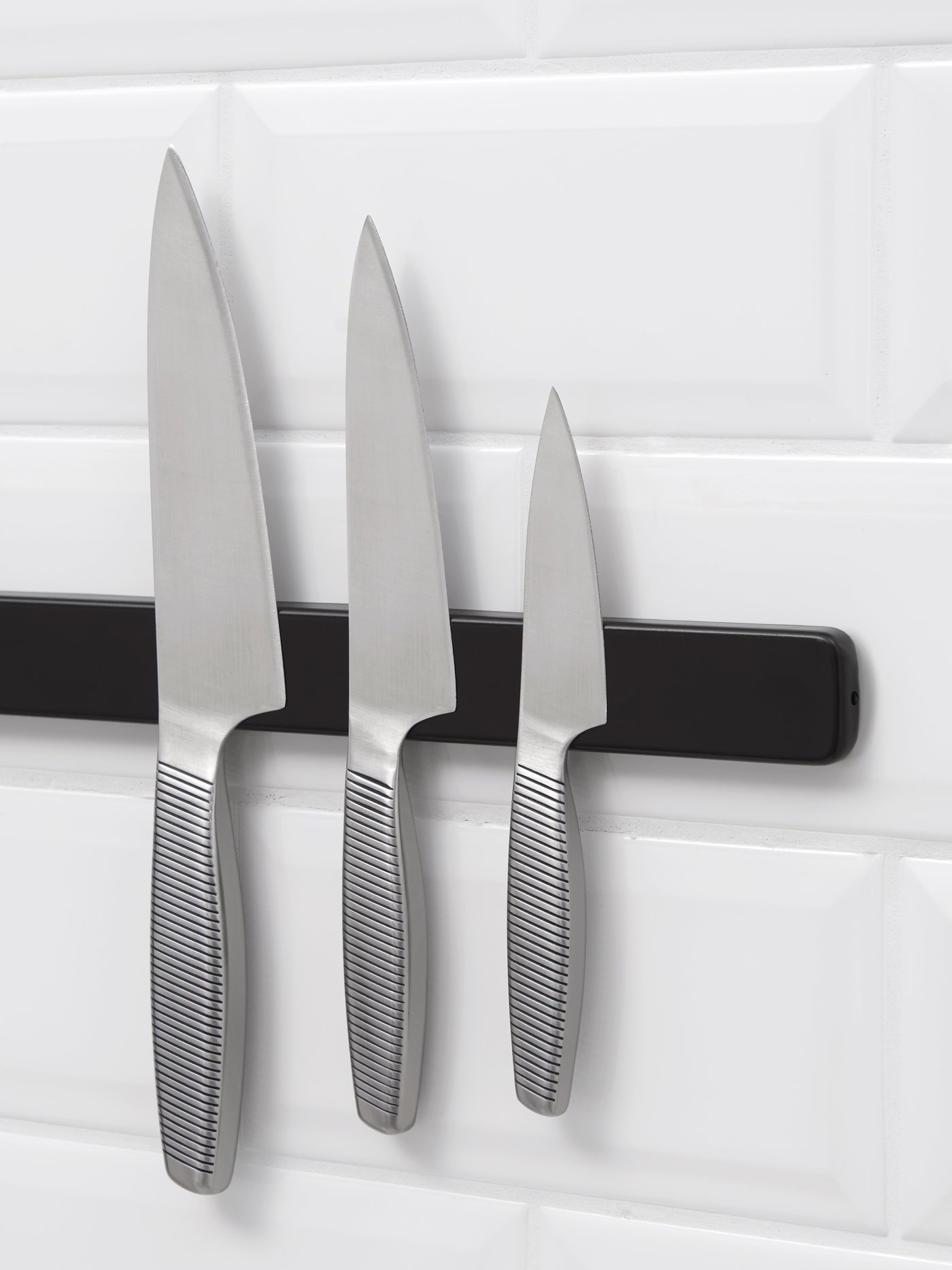 Et knivsæt med tre IKEA 365+ hænger på en magnetskinne i et køkken.