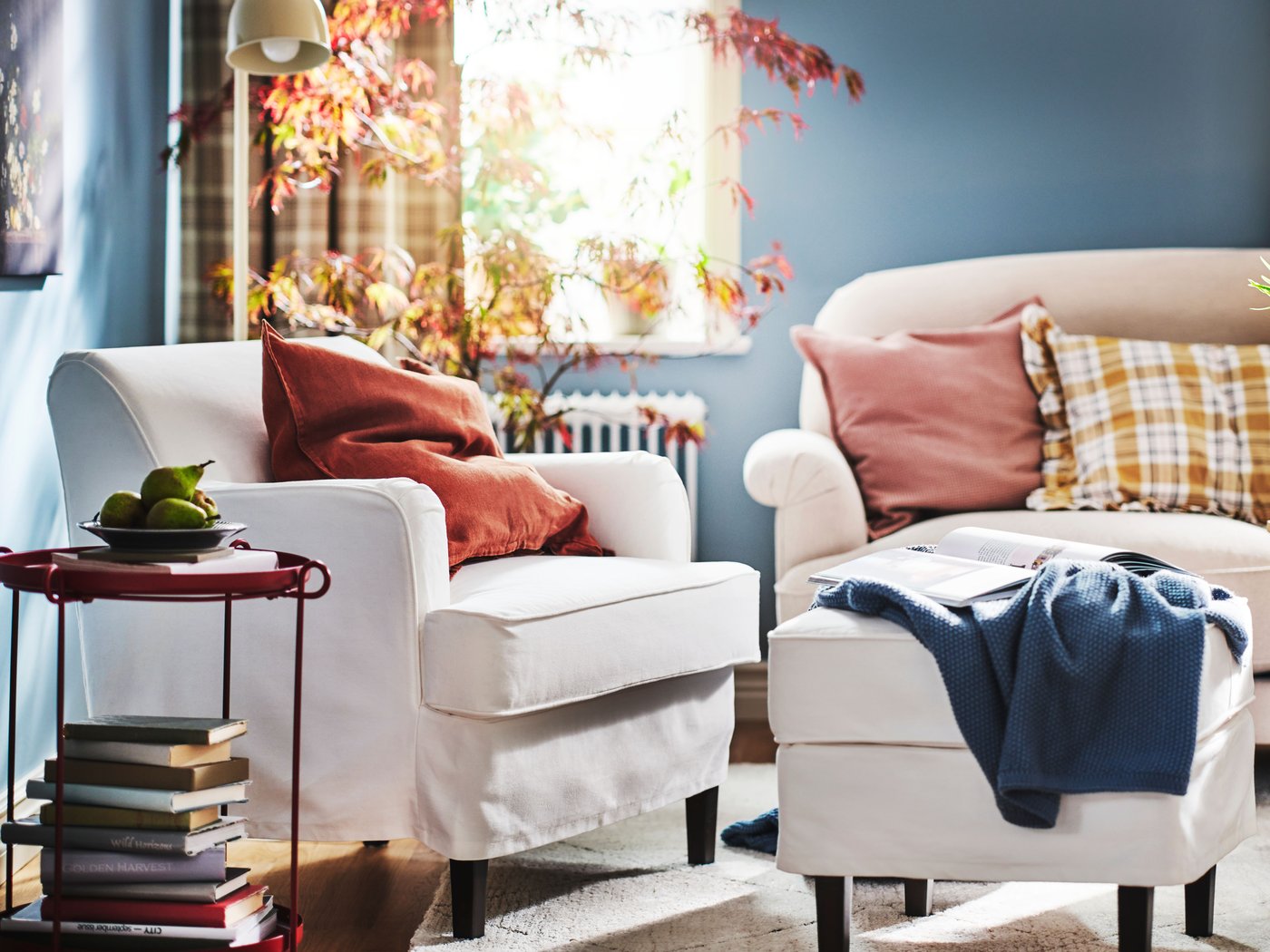 A living room with a white armchair with throws and cushions.