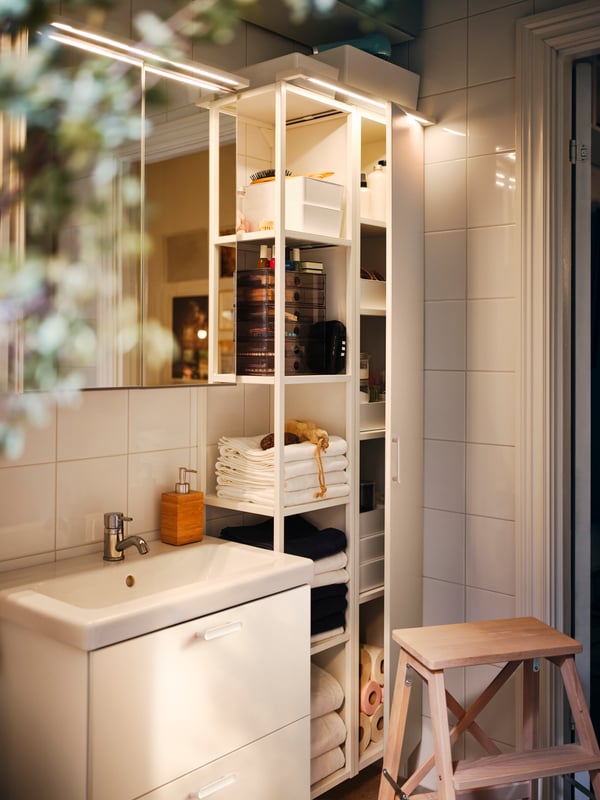 Un baño pequeño con muebles para baño ENHET. Uno es un mueble para lavamanos con dos puertas blancas y al costado una repisa abierta con una puerta.