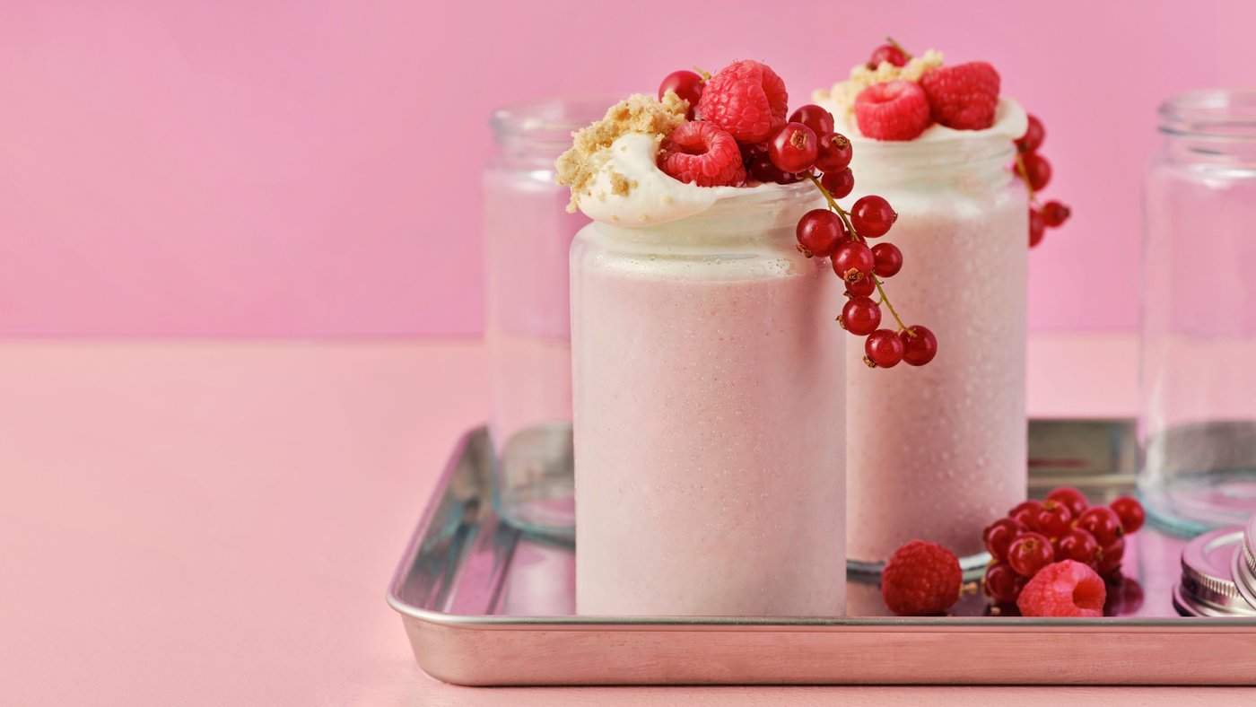 Zwei LÅNGLUR Obstsmoothie-Milchshakes sind mit roten Himbeeren, roten Johannisbeeren und Keksbröseln garniert.
