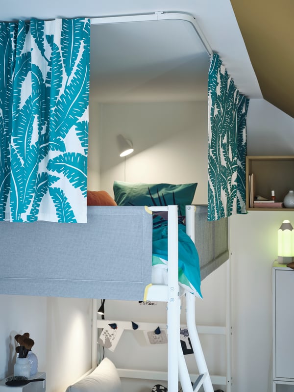 The top of a VITVAL loft bed is surrounded by curtains made from UGGLEMOTT fabric hanging from VIDGA track rails.