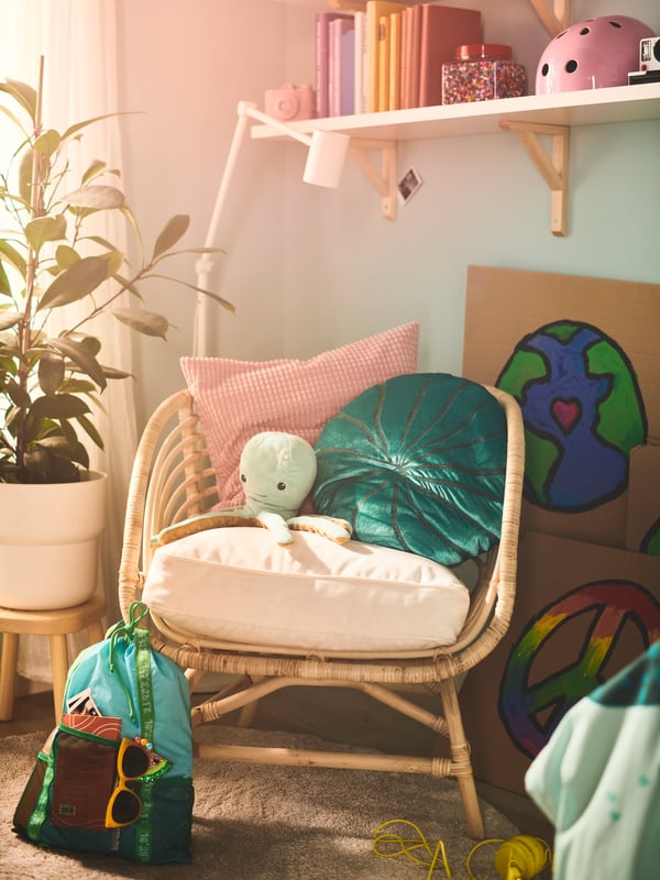 A BLÅVINGAD coral-shaped cushion is on rattan armchair with a BLÅVINGAD octopus night-light in a warmly lit bedroom corner.