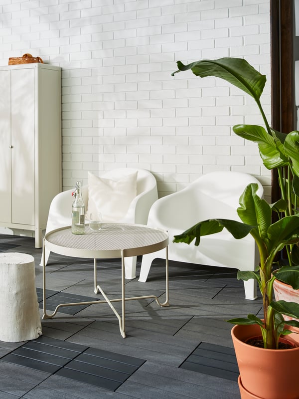 Una terraza con dos sillones de exterior y una mesa KROKHOLMEN, todo en blanco. Al costado derecho de la terraza hay una planta alta n una maceta de greda.