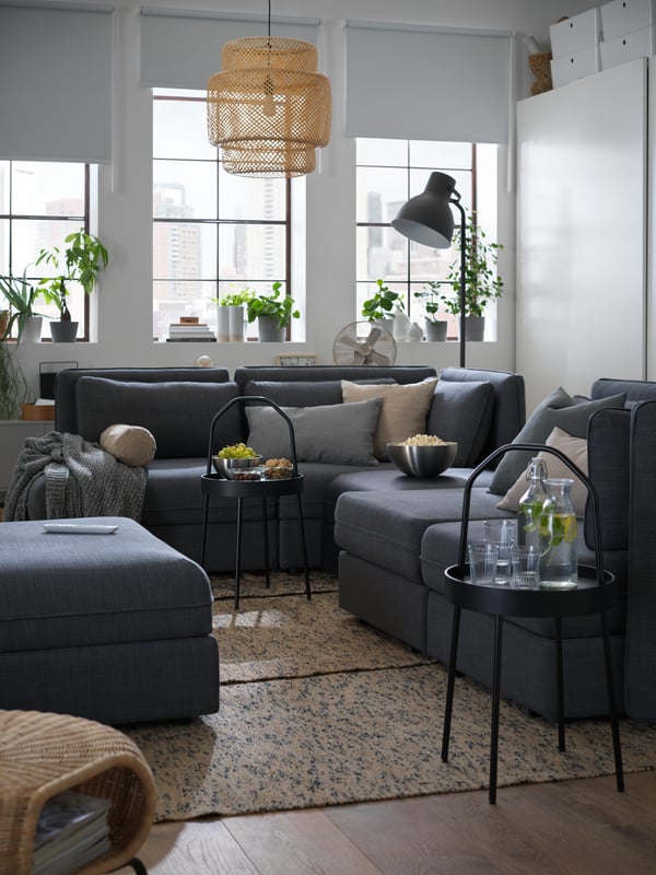 Un grand canapé modulaire VALLENTUNA et deux tables dʼappoint BURVIK noires sur lesquelles sont posées des boissons et des collations, dans un appartement dʼune pièce.