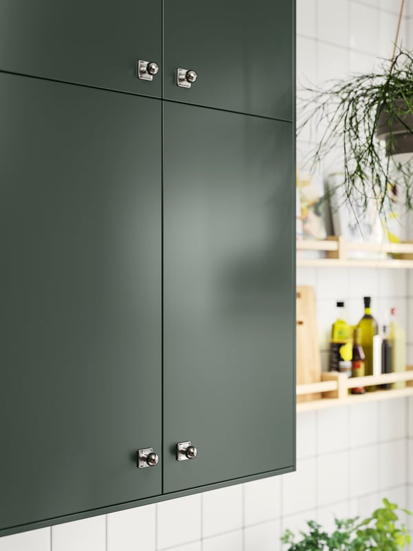 Wall cabinets with deep green HAVSTORP kitchen fronts and stainless steel SÖRBYN knobs, on a white-tiled wall.
