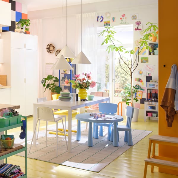A bright kitchen featuring vibrant decor, a white VIHALS wooden table, small children’s table and potted plants.