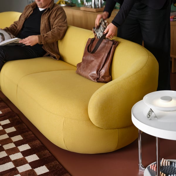 A person reaches into a bag that is laying against the backrest of a LILLESÄTER 6-seat sofa in Gunnared bright green-yellow.