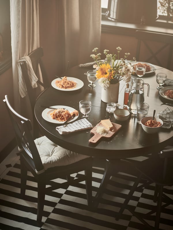 Mesa extensible negra INGATORP con platos con comida encima y sillas negras INGOLF.