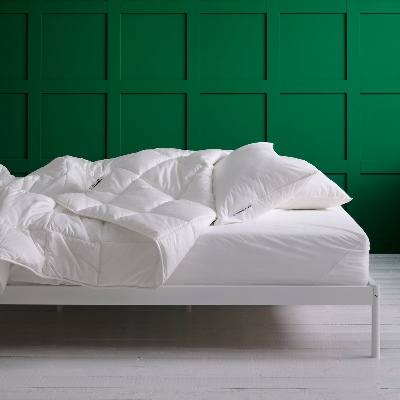 Una cama blanca con un duvet esponjoso y almohadas sin fundas frente a una pared verde.