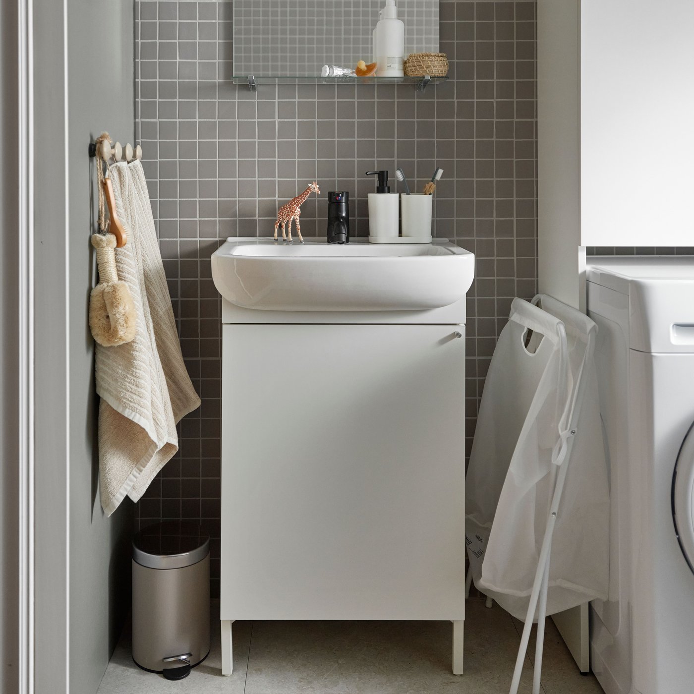 Et hvidt NYSJÖN skab til vask er placeret ved siden af et toilet i et badeværelse med mørke vægge og hvidt gulv med prikker.