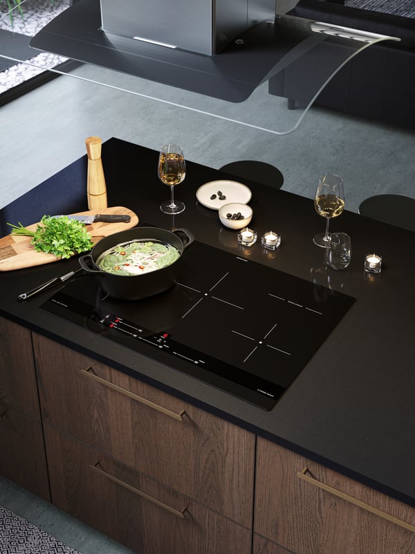 An induction cooktop on the kitchen island with a black cooking pot and an extractor hood on the ceiling.
