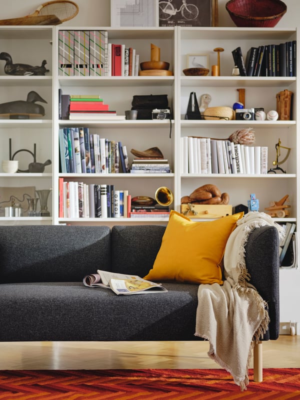Dark grey LILLEHEM sofa with yellow GURLI cushion and cover on top in front of a row of BILLY bookcases.