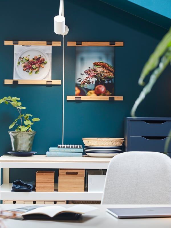 Two VISBÄCK poster hangers in bamboo with food posters hang on a wall, and a white wall lamp illuminates.