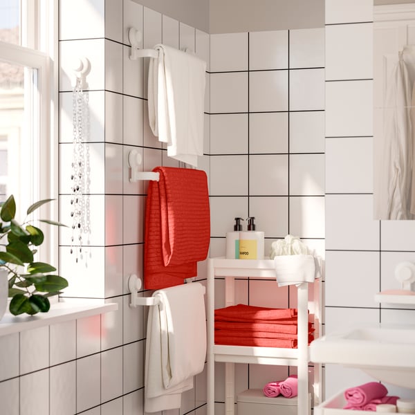 Three VÅGSJÖN cotton towels in red and white hanging on three TISKEN towel racks with suction cup in a white tiled bathroom.
