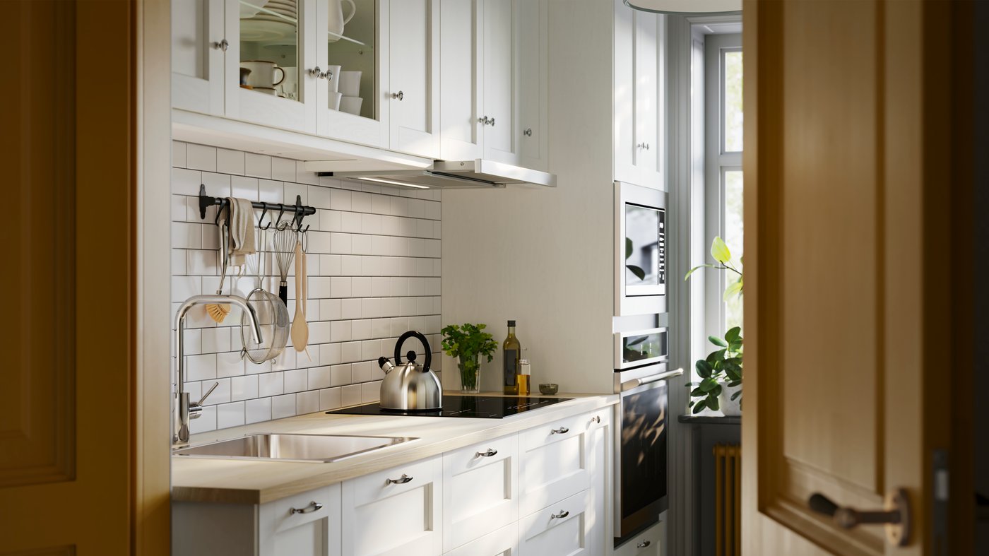 A kitchen has drawers and wall cabinets with white ENKÖPING fronts and a nickel-plated HULTARP rail with hooks on the wall.