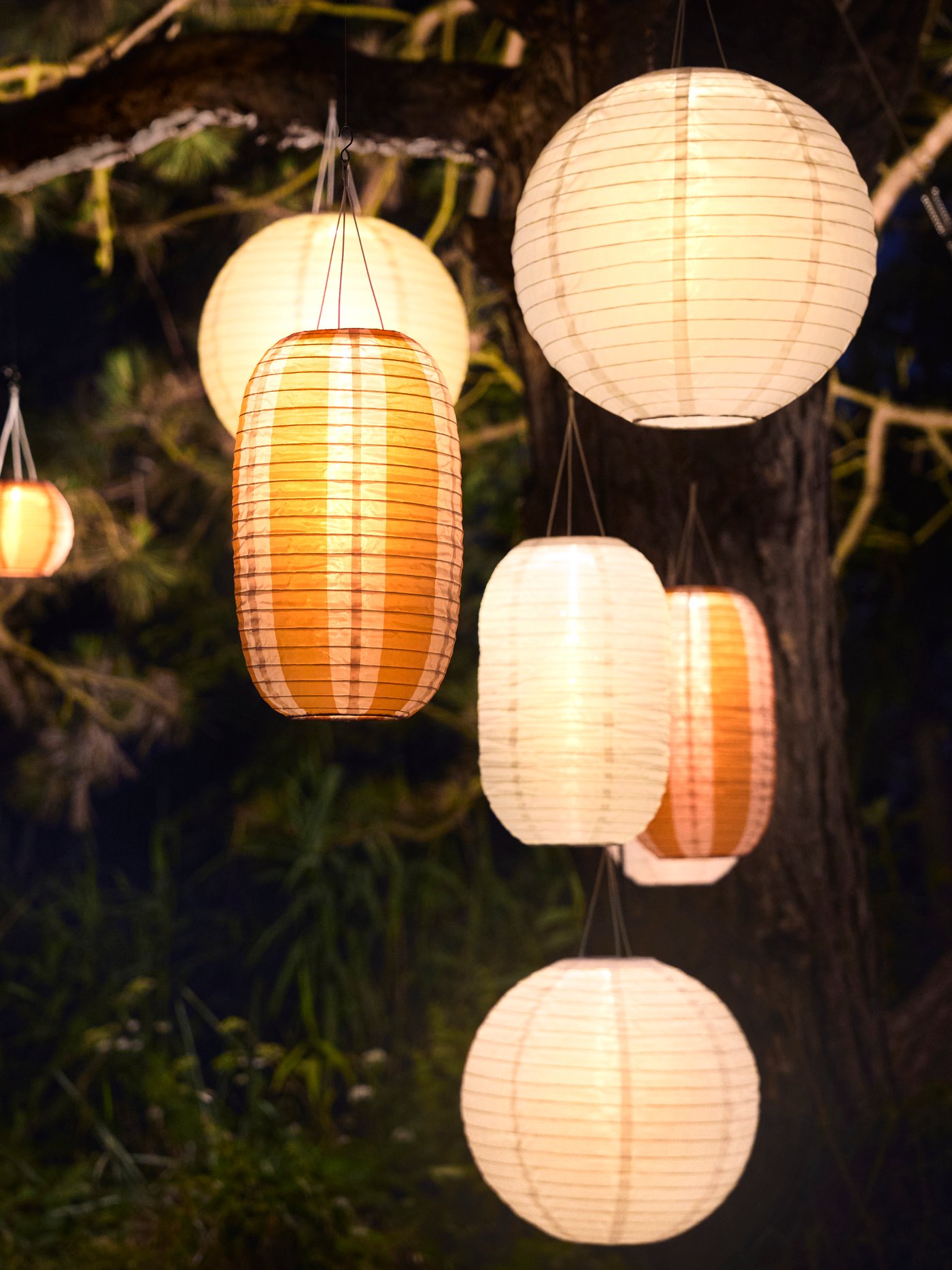 An outdoor area is illuminated by many white and striped orange SOLVINDEN pendant lamps that enhances the ambiance.