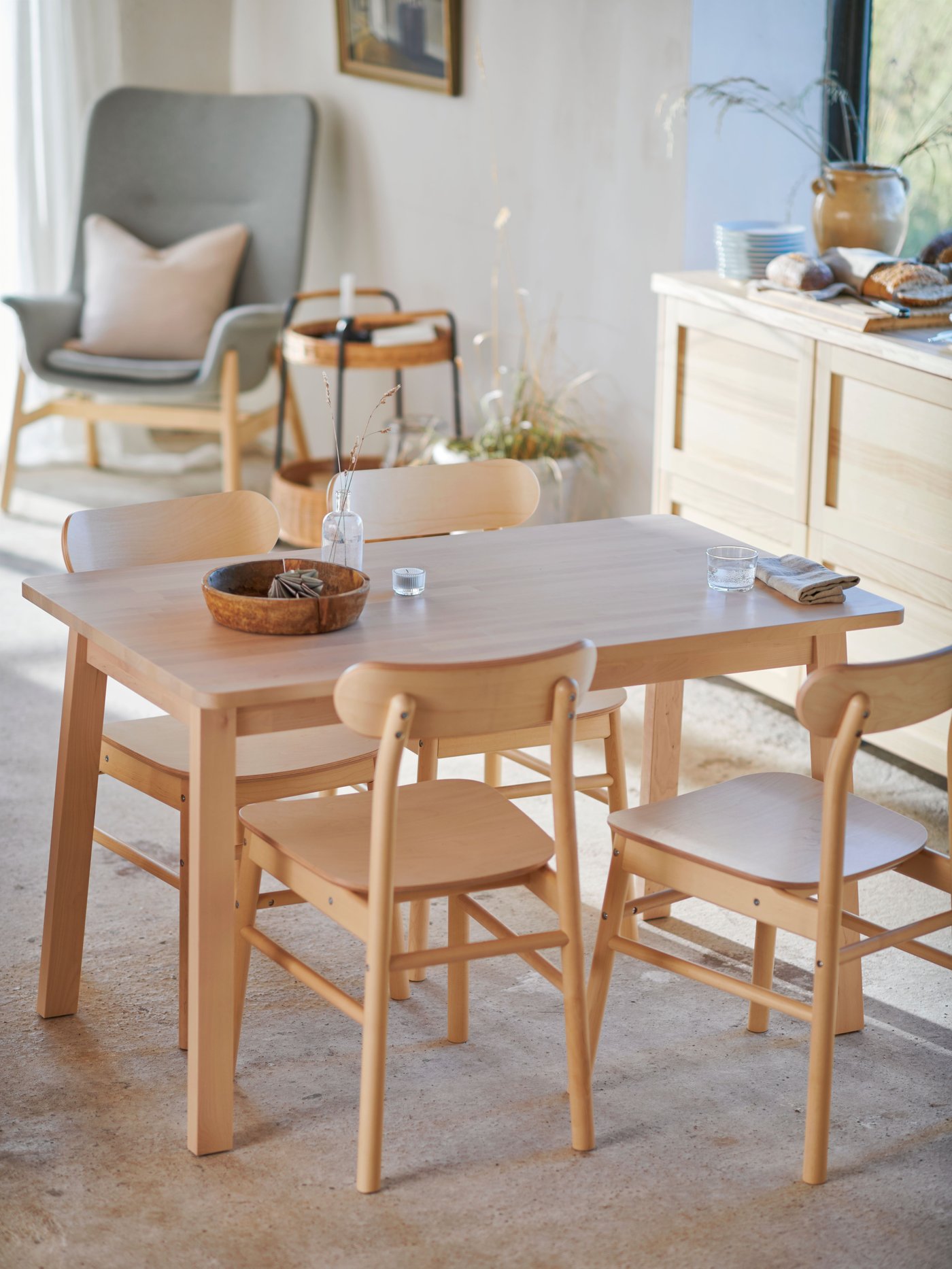 A dining area with a rustic feel with concrete floors and four RÖNNINGE chairs in birch placed around a NORRÅKER table.