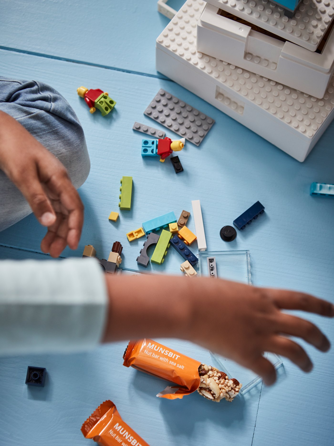 A child playing on the floor, building blocks in different colours and two MUNSBIT nut bars, one of them half-eaten.