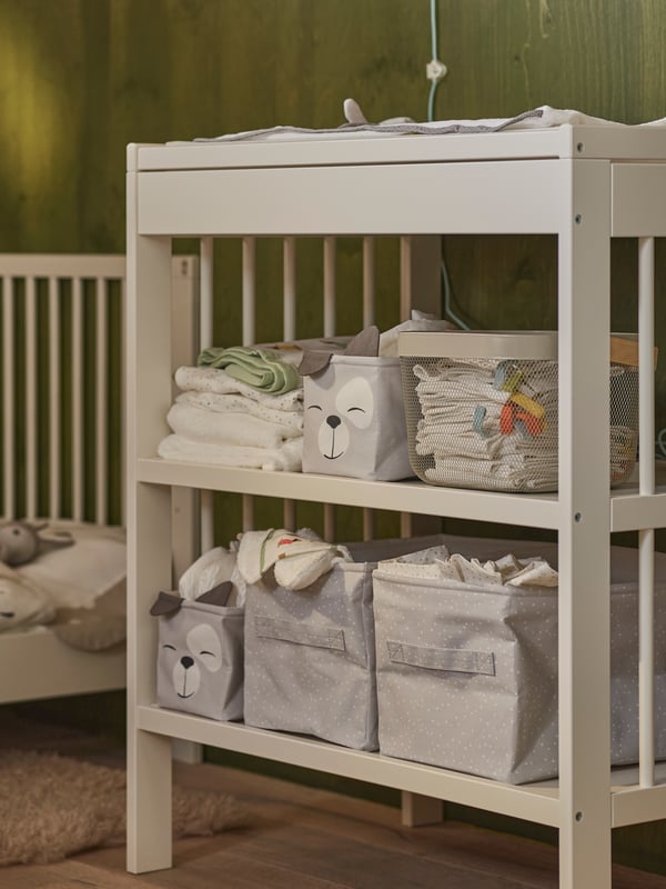 Two sets of DRÖMSLOTT boxes on two shelves of a white GULLIVER changing table, alongside other baby textiles and a basket.