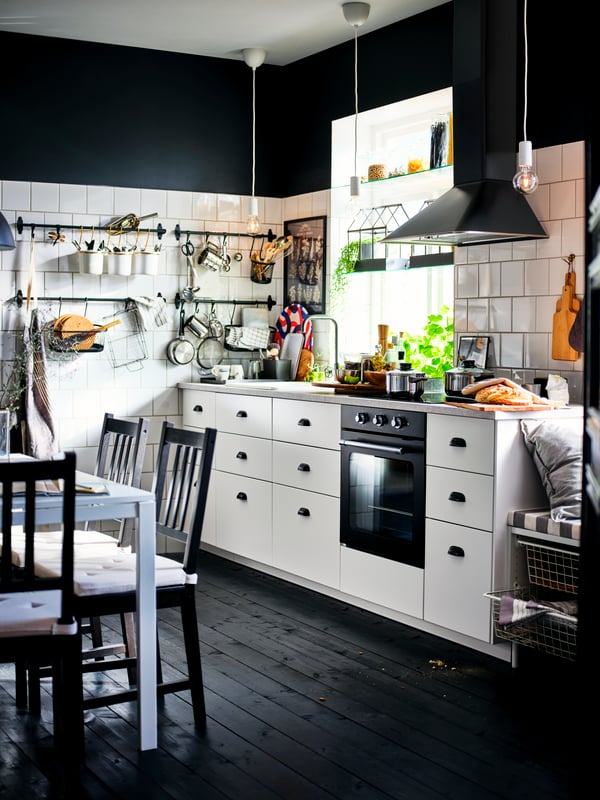 A black-and-white kitchen with white METOD cabinets with MAXIMERA interiors, a black extractor hood and a dark wood floor.