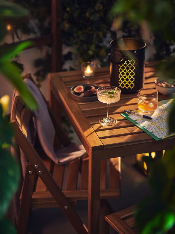 An evening setting with dim lighting, a NAMMARO table is in focus displaying a lantern and different tableware and snacks.