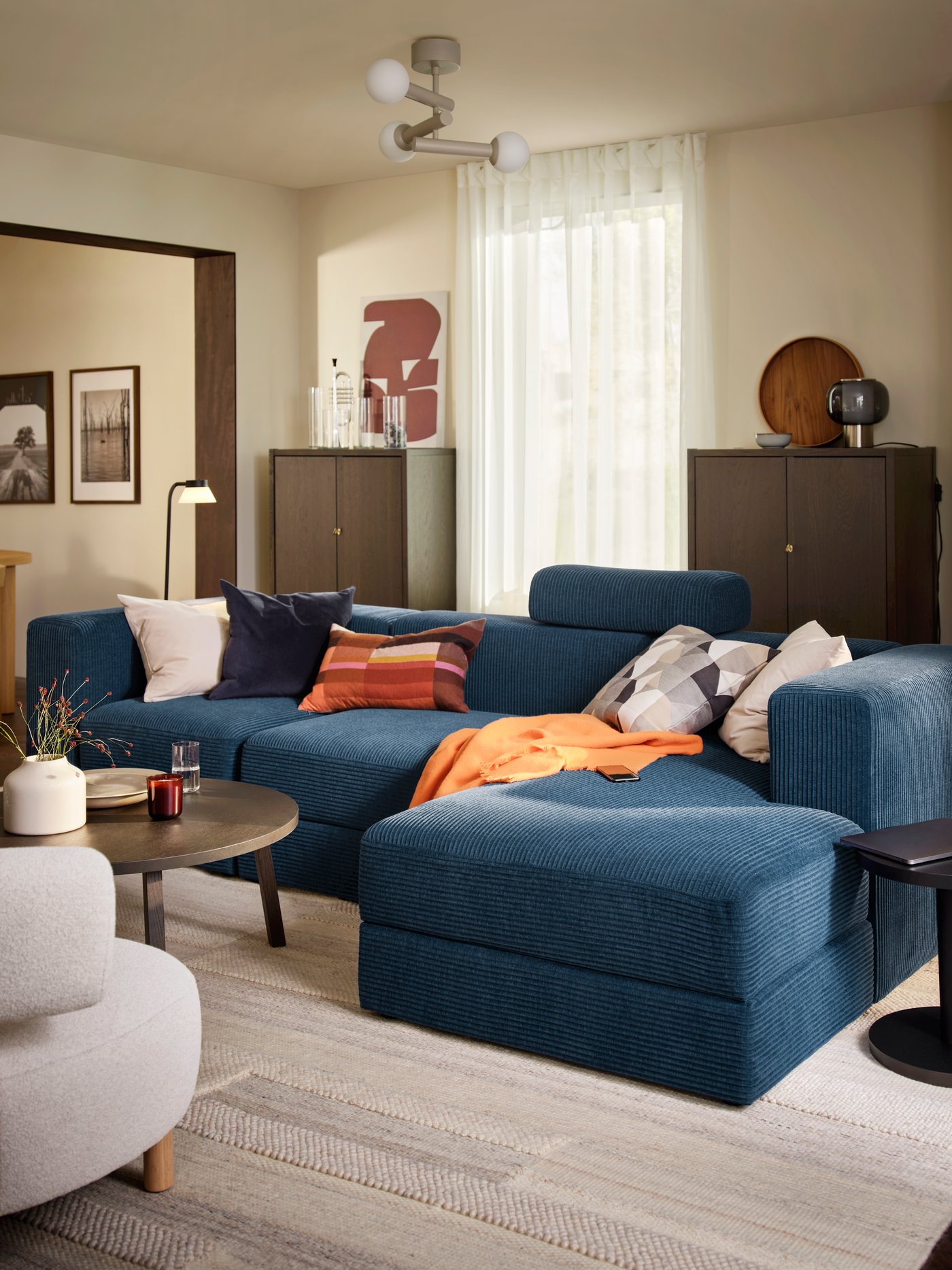 A living room with a dark-blue JÄTTEBO four-seat sofa with chaise longue, complemented by a round table and decorative items.