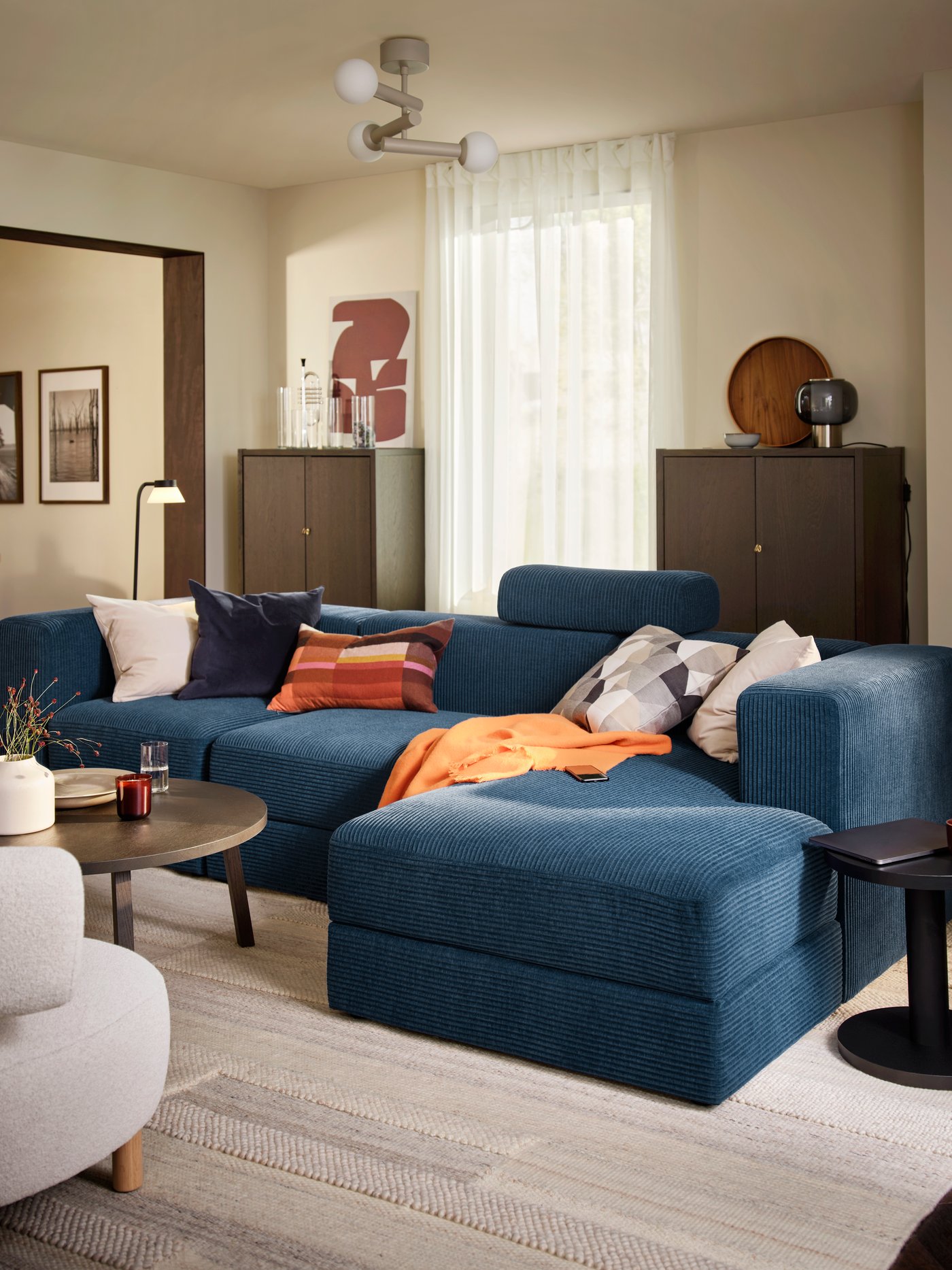 A living room featuring a dark blue JÄTTEBO 4-seat sofa with chaise longue, paired with a round table and decorative home accessories.