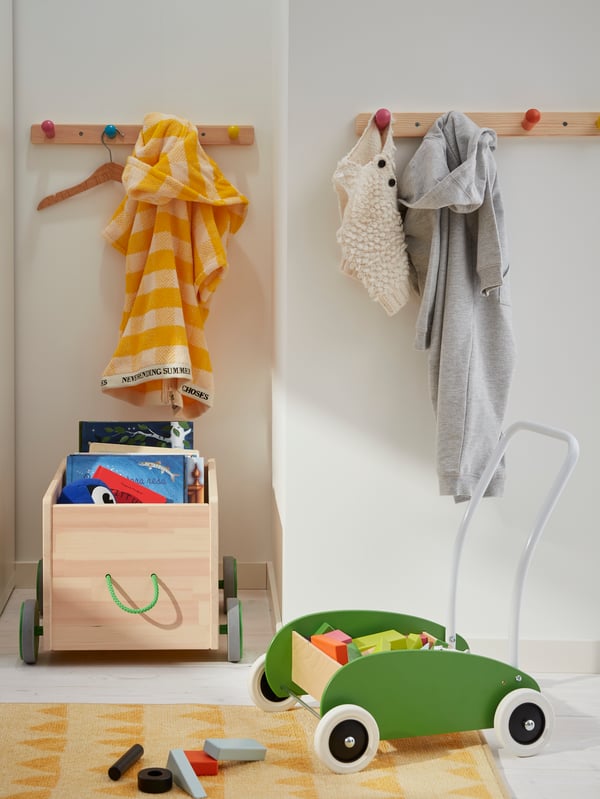Salle de jeu avec patères à boutons et wagons IKEA en bois remplis de jouets.