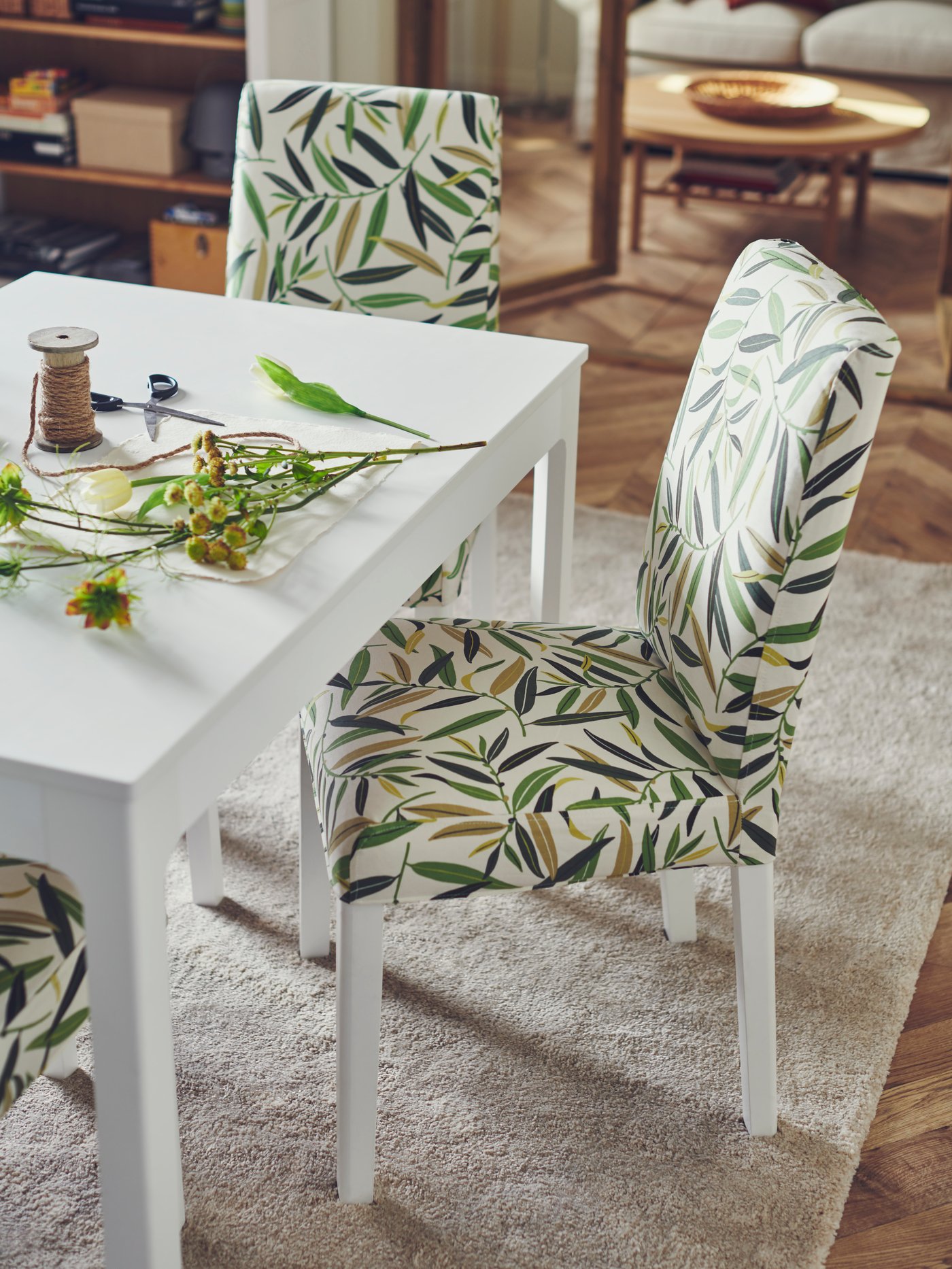 In a dining room with a white dining table, two IKEA BERGMUND dining upholstered chairs with white legs and a leaf pattern cover.