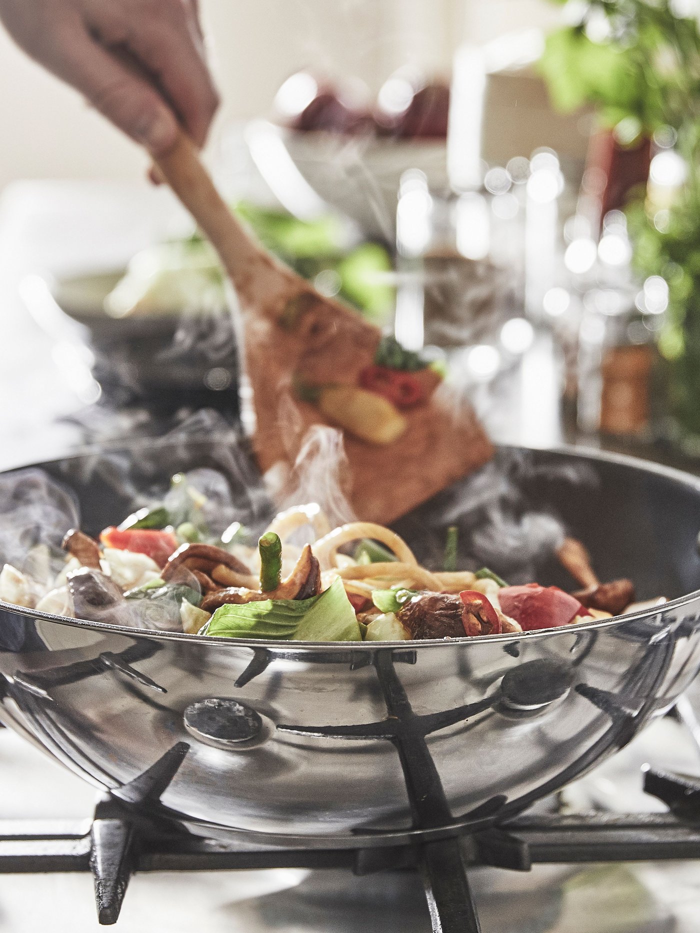 Someone cooking vegetables with a wooden spoon on an IKEA MIDDAGSMAT silver wok.
