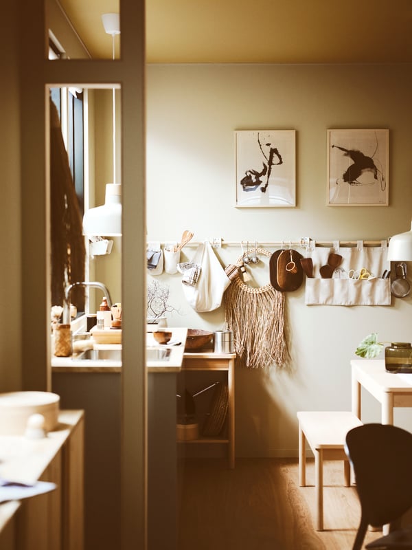 A kitchen and dining area with a RÖNNINGE trolley, and two framed prints with rails below with a NEREBY hanging organiser.