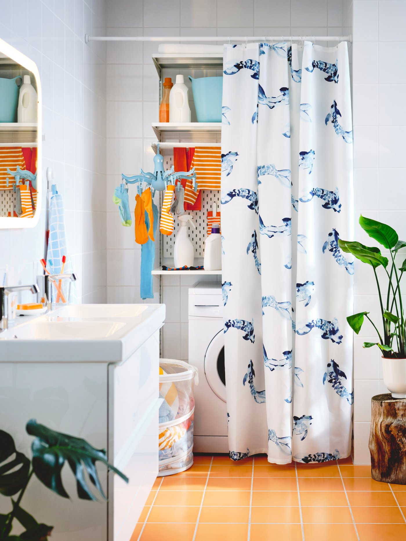 Repisas blancas BOAXEL instaladas a muro detrás de una cortina de baño blanca con patrones azules. Sobre las repisas se ven botellas con insumos de lavado y ropa de bebé roja y naranja colgada. 