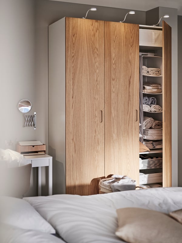 A PAX/TONSTAD wardrobe with an open door showing a SKUBB hanging storage with 6 compartments inside. A bed is in front.
