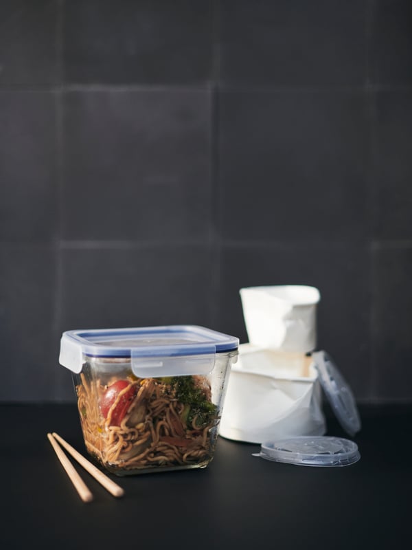 An IKEA 365+ food container holds takeaway noodles, with a discarded disposable container in the background.