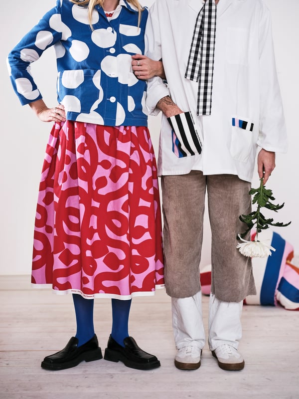 Two people stand arm in arm dressed in clothes made from the Tyg collection. The skirt is in FLUGBLOMSTER pre-cut fabric.