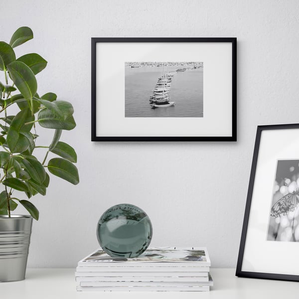 Jedan LOMVIKEN okvir postavljen je na zid, a drugi se nalazi na klupi, pored časopisa i biljke.