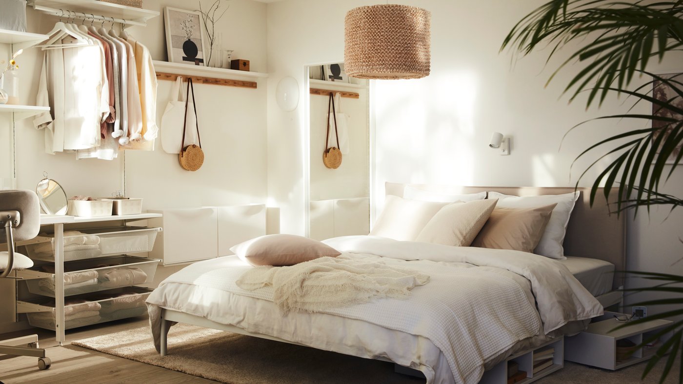 Un dormitorio soleado con una cama KLEPPSTAD con ropa de cama blanca ÄNGSLILJA y una lámpara LERGRYN colgada encima.
