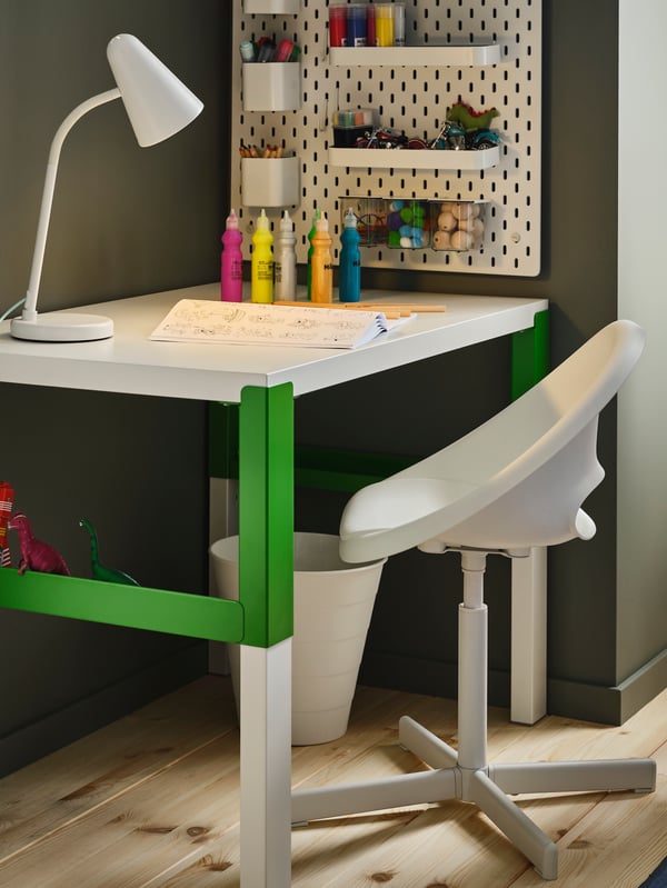 A PÅHL desk with LOBERGET/SIBBEN chair and a pegboard on the wall. A lamp, book, paints and pencils are on the desk.