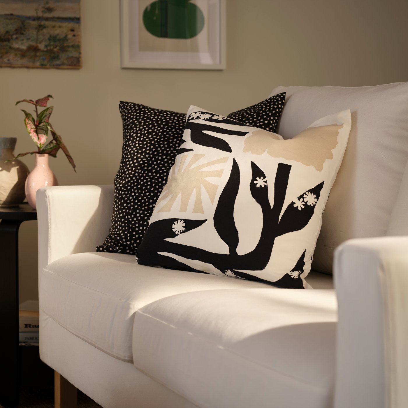 A living room with a softly sunlit, white SALTSJÖBADEN two-seat sofa with patterned DRABOR and BJÖRKGRÅMAL cushion covers.