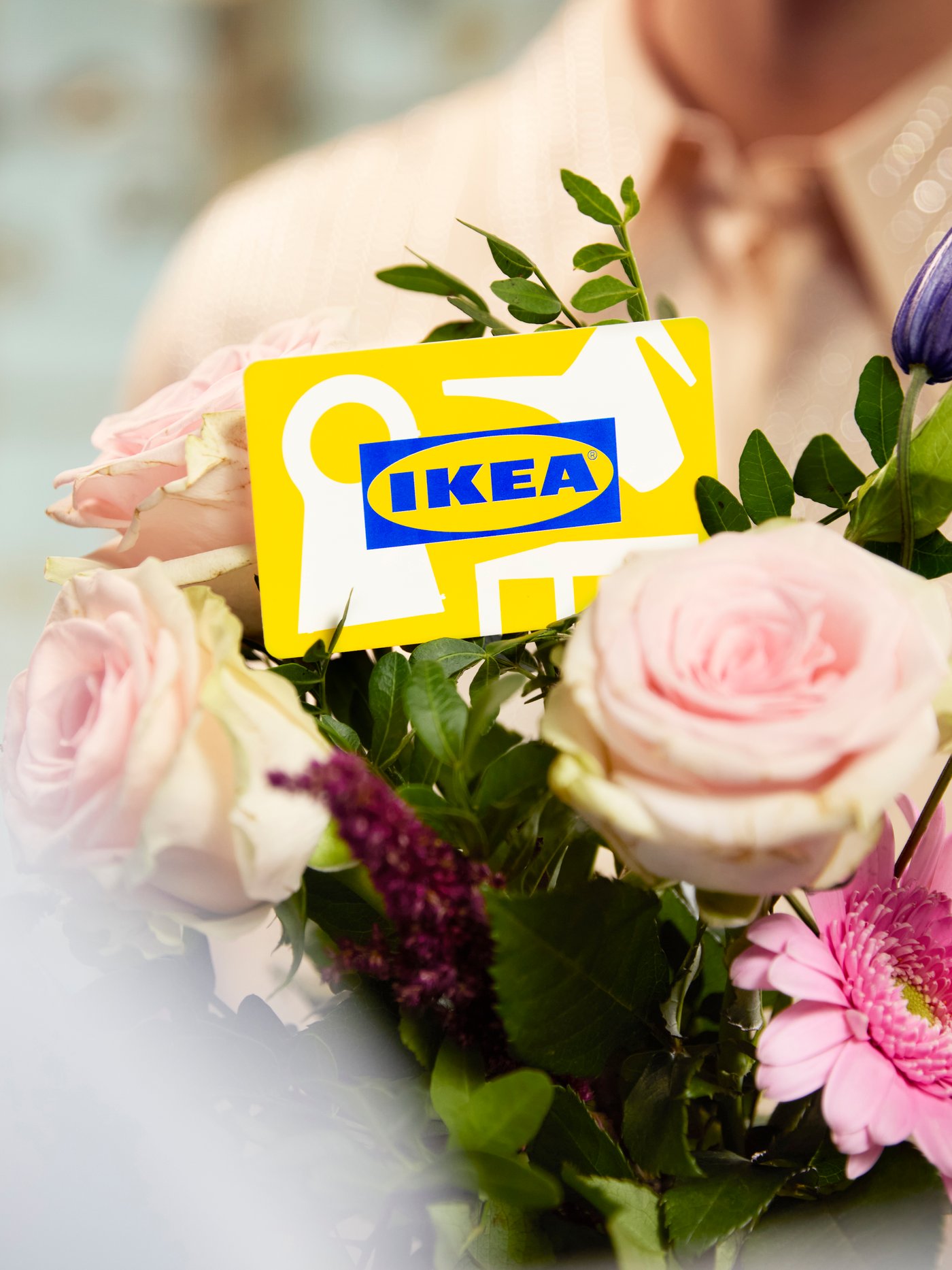 Bukett med rosa blommor där ett presentkort hålls fram framför arrangemanget.