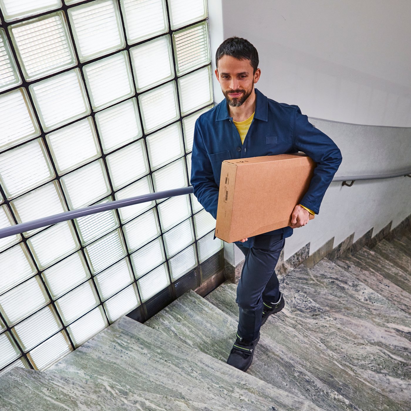 A delivery driver is carrying a parcel up some stairs
