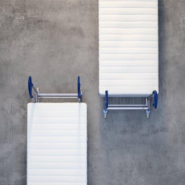 Two IKEA trolleys with mattresses, shot from above against a grey concrete floor.