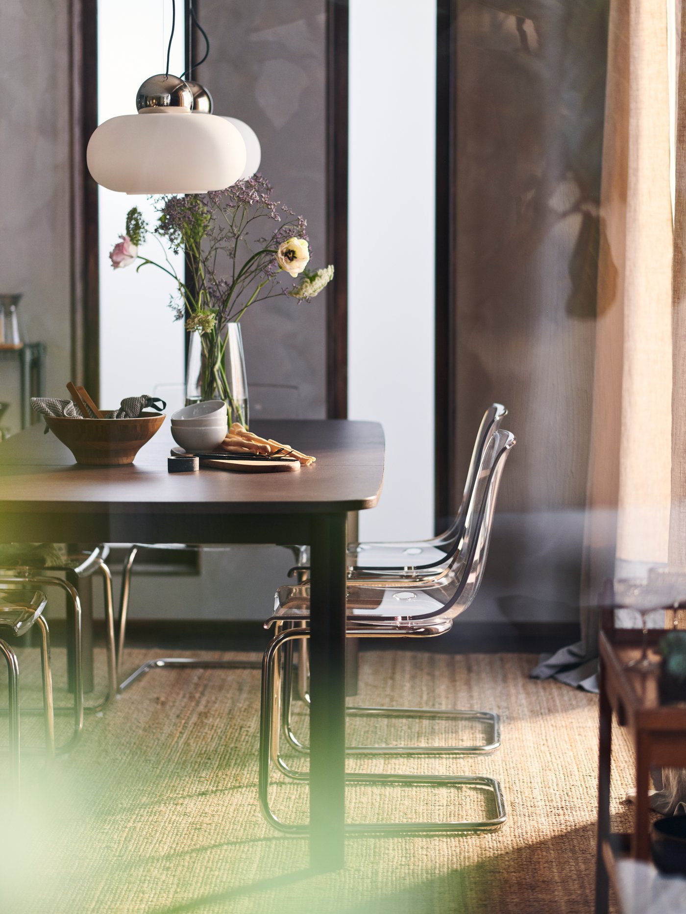A STRANDTORP extendable table in a bright room with TOBIAS chairs around it and two white DEJSA pendant lamps overhead.
