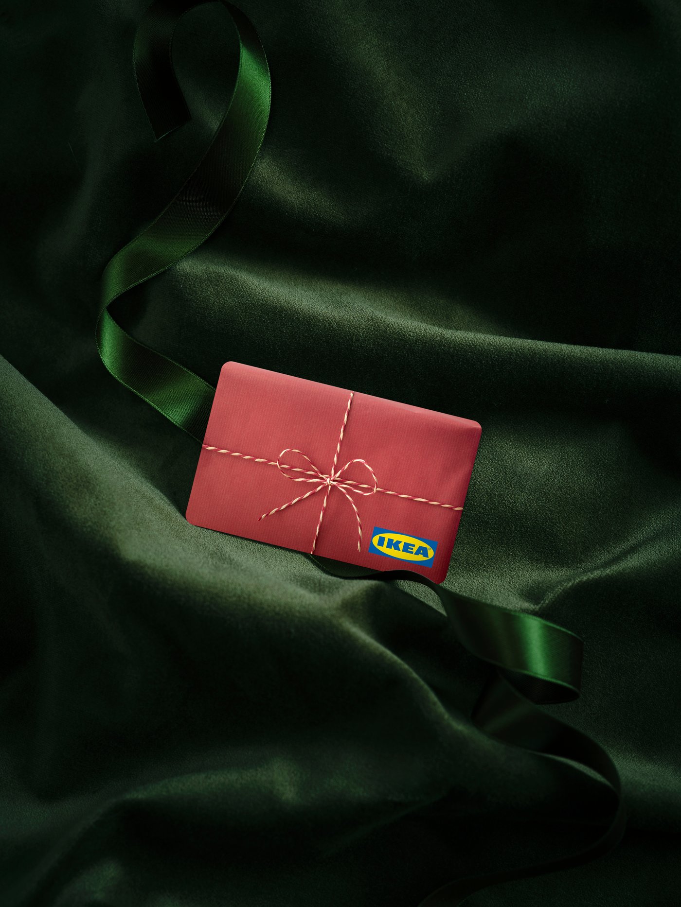 Crvena IKEA poklon-kartica sa slikom ukrasne mašnice i IKEA logotipom na zelenoj somotskoj tkanini.