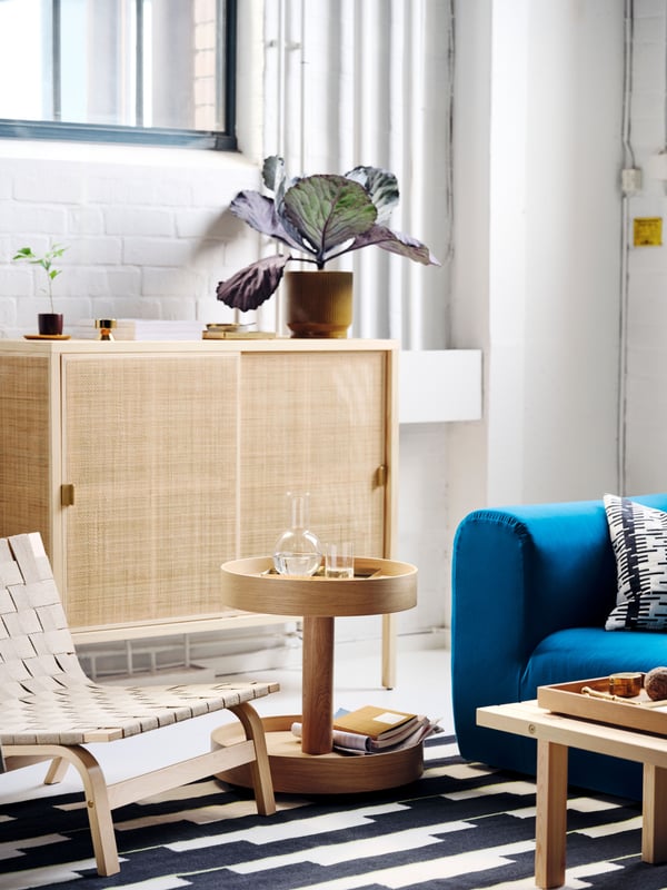 A STOCKHOLM 2025 side table on castors with a carafe and glasses on it, on a rug between a sofa and an easy chair.