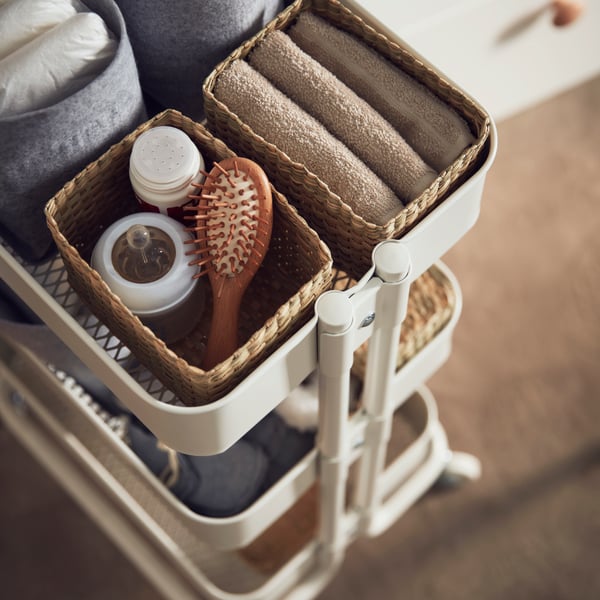 Carrito RÅSKOG con cajas en sus bandejas. Dentro de las cajas hay accesorios de baño como cepillos de pelo, toallas y otros artículos de baño.