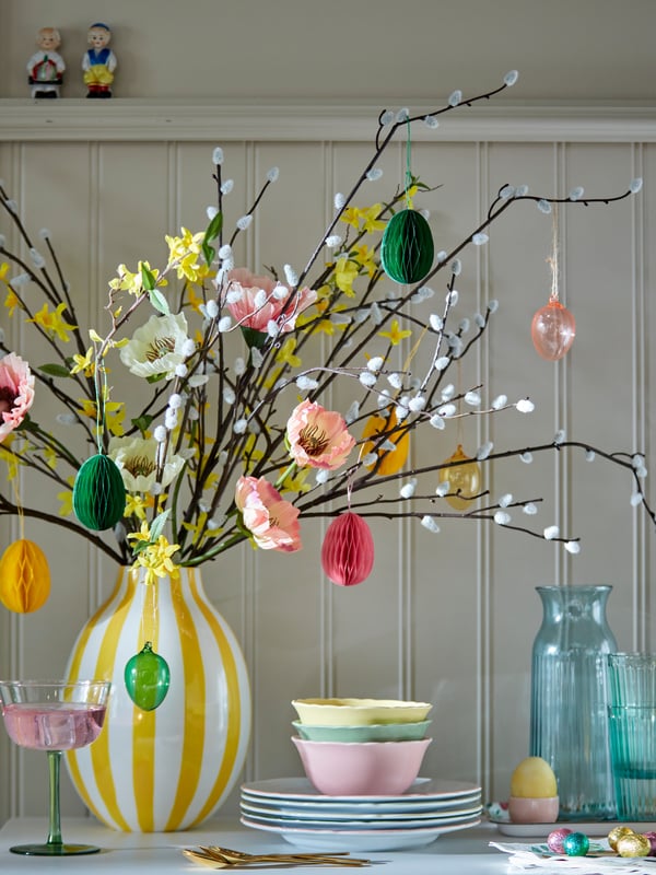 An Easter bouquet of artificial flowers and Easter branches in a yellow‑and‑white striped BLODBJÖRK vase on a spring table.