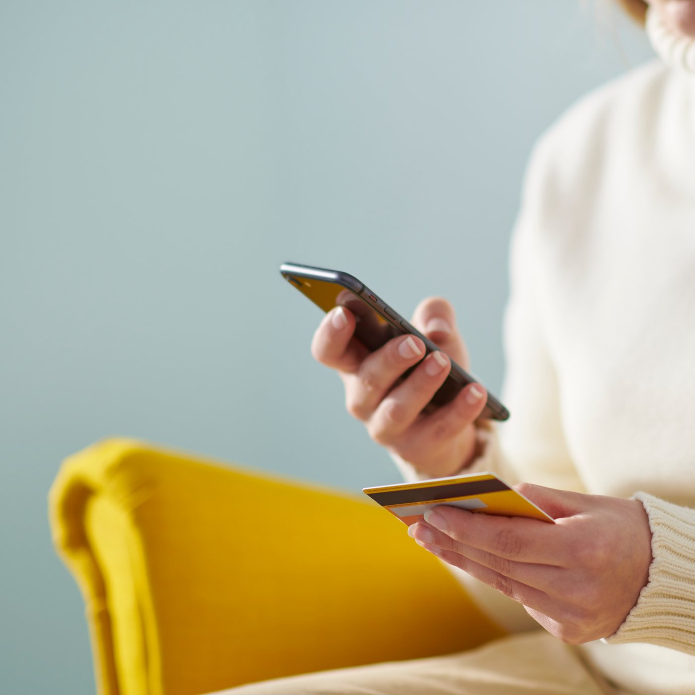 Inimene istub kollasel tugitoolil, käes krediitkaart ja telefon.