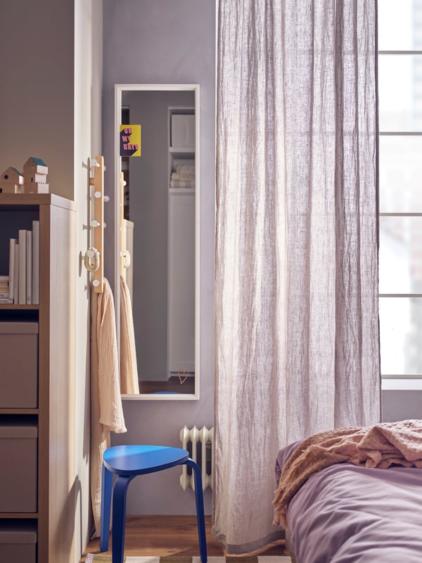 Miroir NISSEDAL blanc fixé au mur à côté d’un rideau DYTÅG gris clair et derrière un tabouret KYRRE bleu vif.