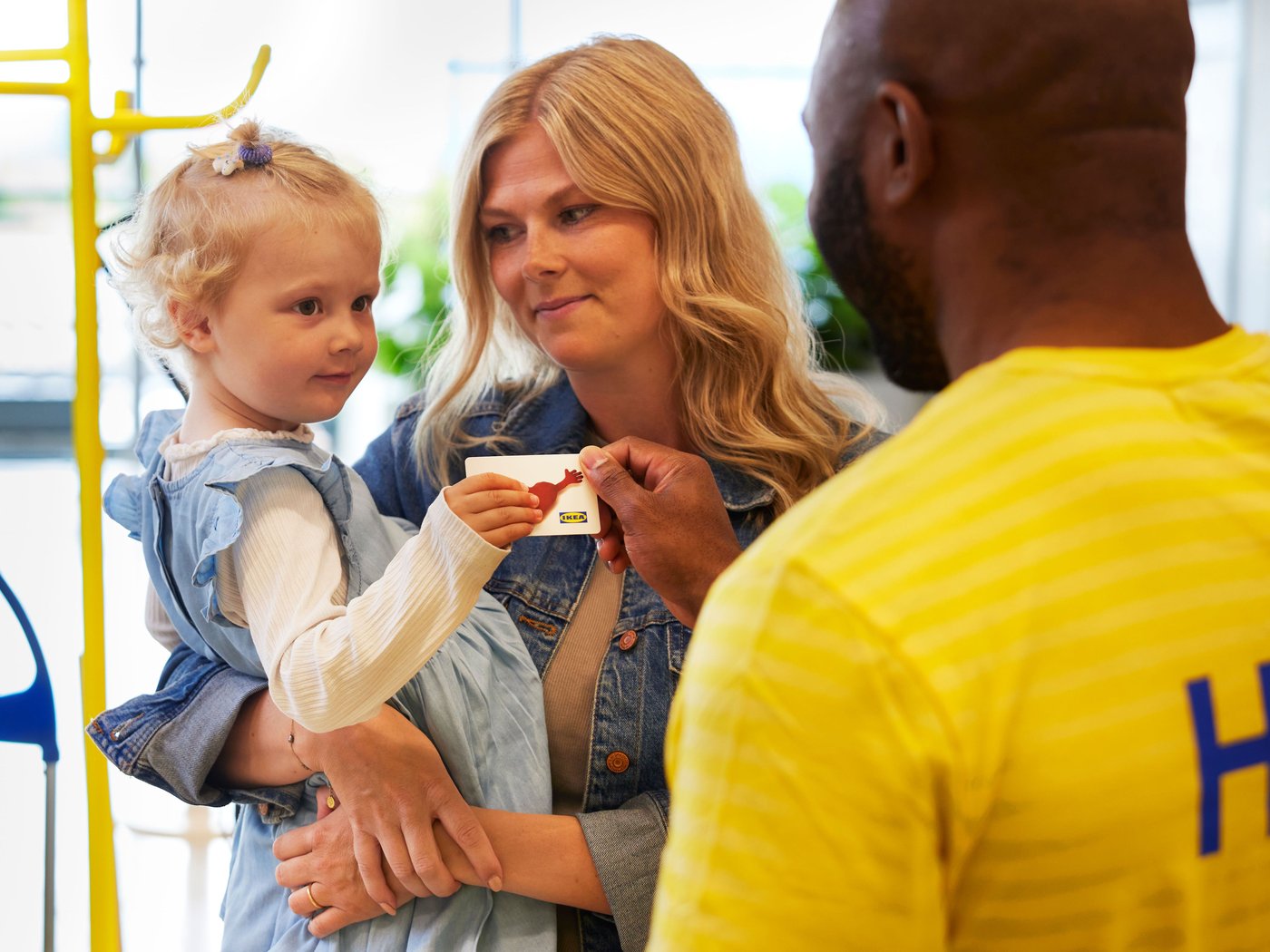 Un collaborateur tend une carte-cadeau IKEA à une femme avec son enfant.